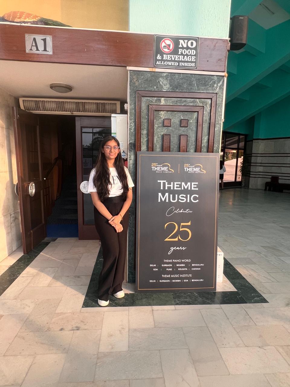 Priyal standing beside the Theme Music Celebrates 25 Years sign at the concert venue
