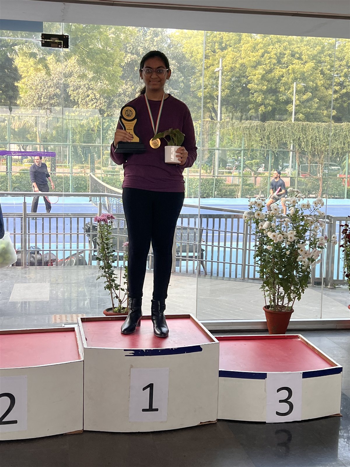 Priyal standing on the first-place podium holding her winner's trophy, wearing a gold medal